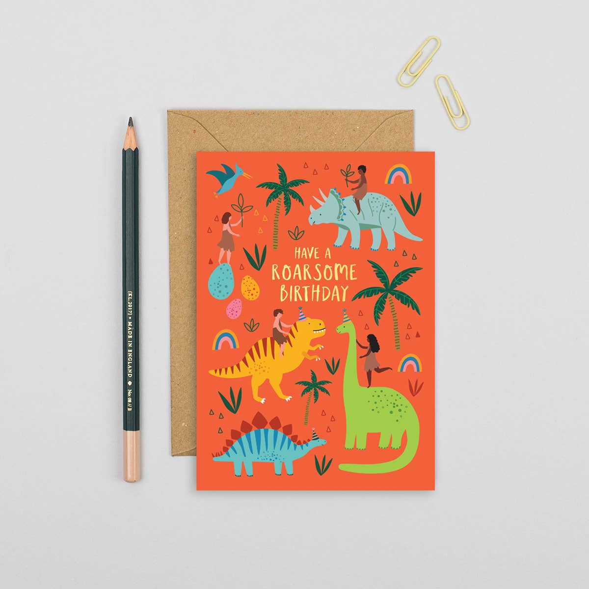 Bright orange birthday card with cartoon dinosaurs, kids riding them, and 'Have a roarsome birthday' text. Eco-friendly, sustainably sourced.