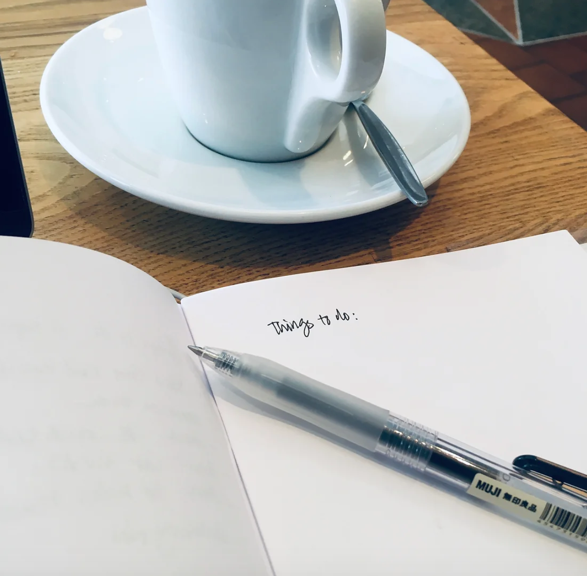 A blank notebook with the words written Things to do with a pen across it on a table with a cup and saucer.