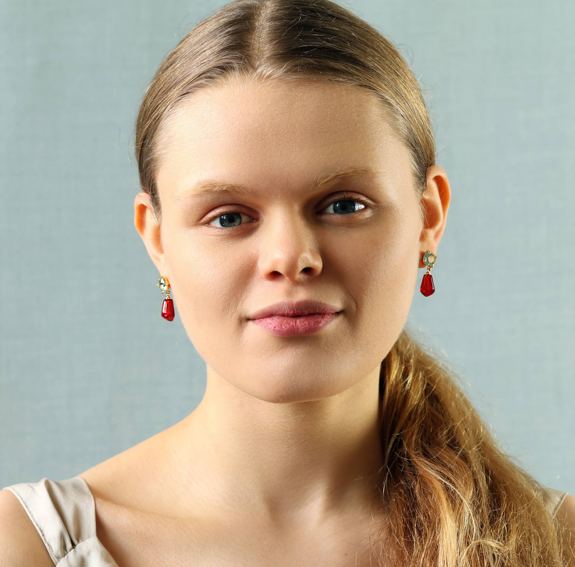 Model wears these sweet and colourful earrings feature a light sapphire blue glass jewel in a delicate, with a bright red pomegranate seed charm beneath.  These earrings have a stud post fastening with butterfly backs. The blue jewels are made from glass and the pomegranate seeds are made from resin. They measure 30mm (just over one inch) in length and are light and comfortable to wear.