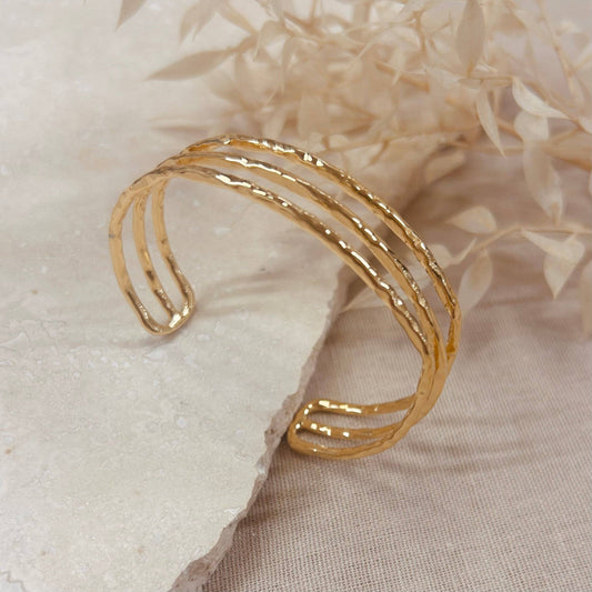 A hammered trio bangle in a polished gold finish. 18k gold plated bracelet. Light and comfortable enough to wear all day, and works well as a stacking piece for a more eye-catching look.