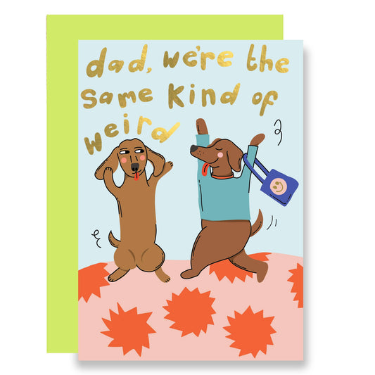 Illustration of two brown dogs dancing around with their tongues out. One is wearing a blue jumper and carrying a blue tote with a smiley face on it. With the words dad, we're the same of weird in gold foil at the top of the card.