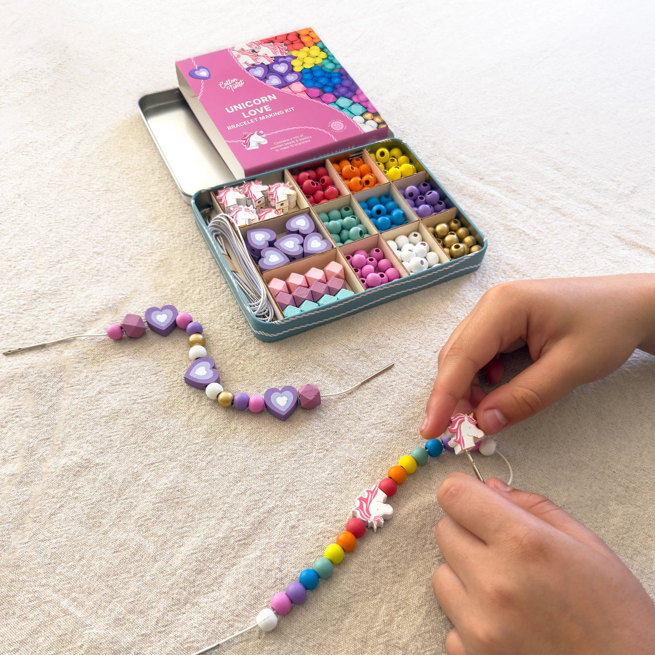 Colourful eco friendly bead kit with a child's hands making a necklace on a light surface
