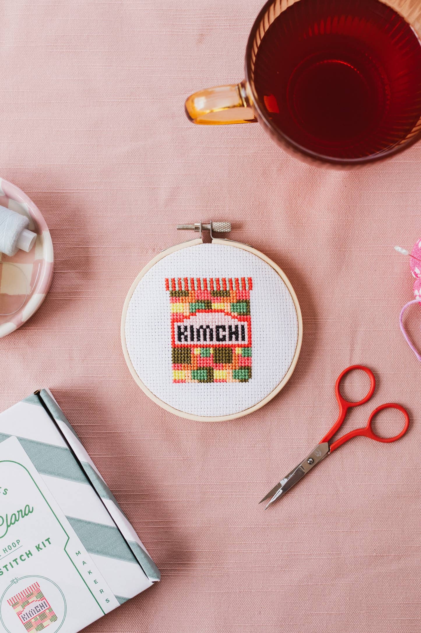 Hand holding the completed Kimchi Mini Cross Stitch in its wooden hoop, ready for display.