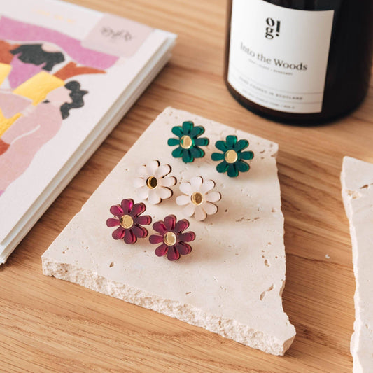 Close-up of a single white daisy stud earring with gold centre on a recycled card.