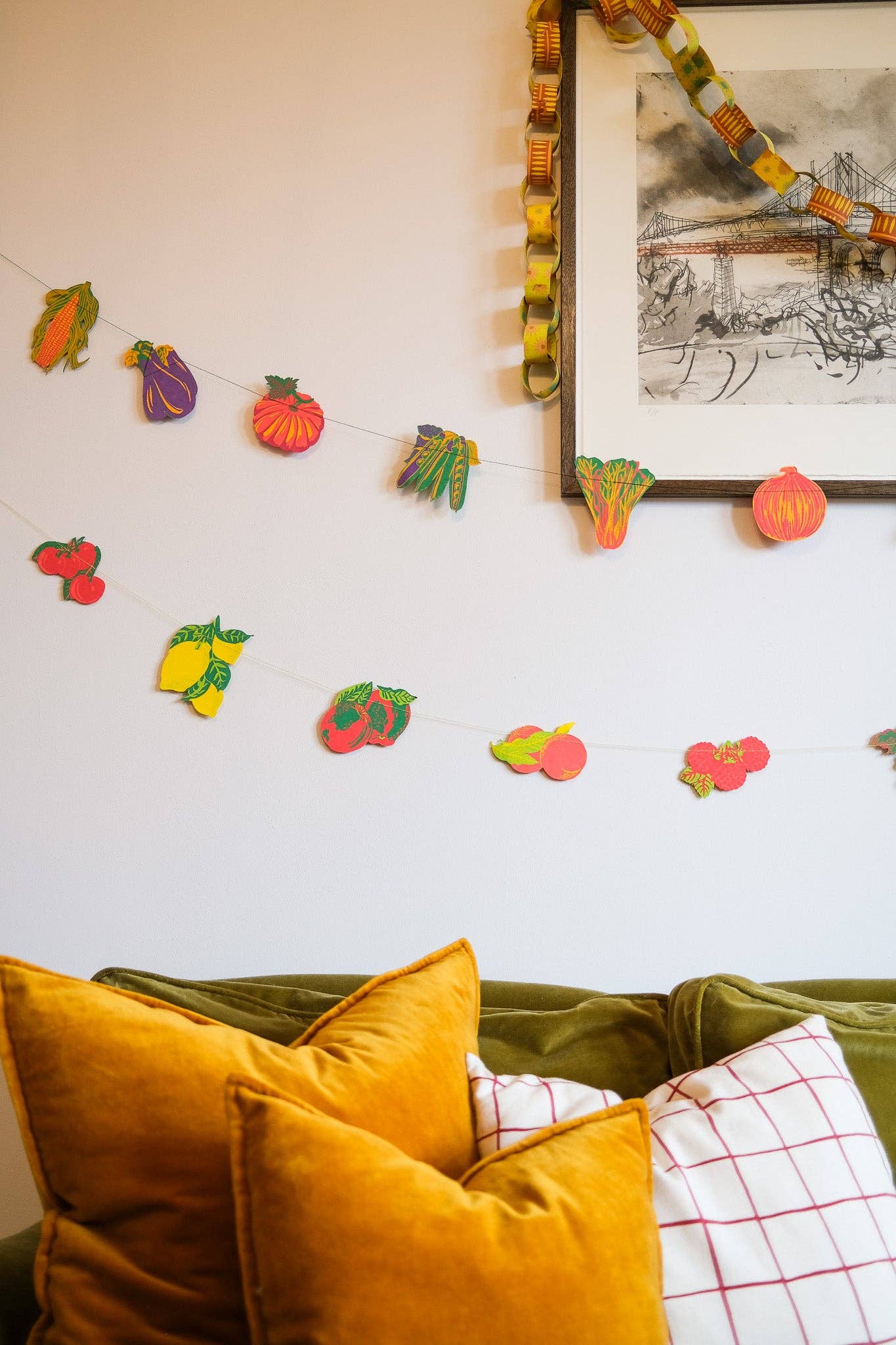Fruit Sewn Garland displayed above a sofa with cushions, featuring hand-printed strawberries, apples, and pineapples, adding cheerful decor.