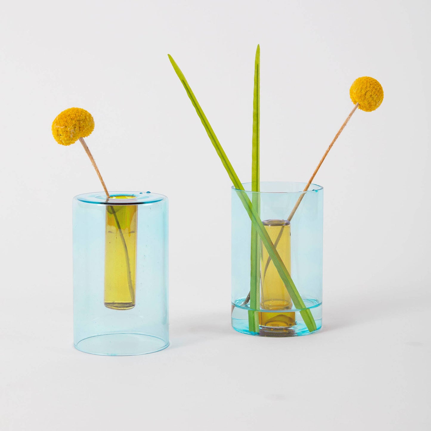 Two blue glass vases with yellow flowers and green stems on a light gray background