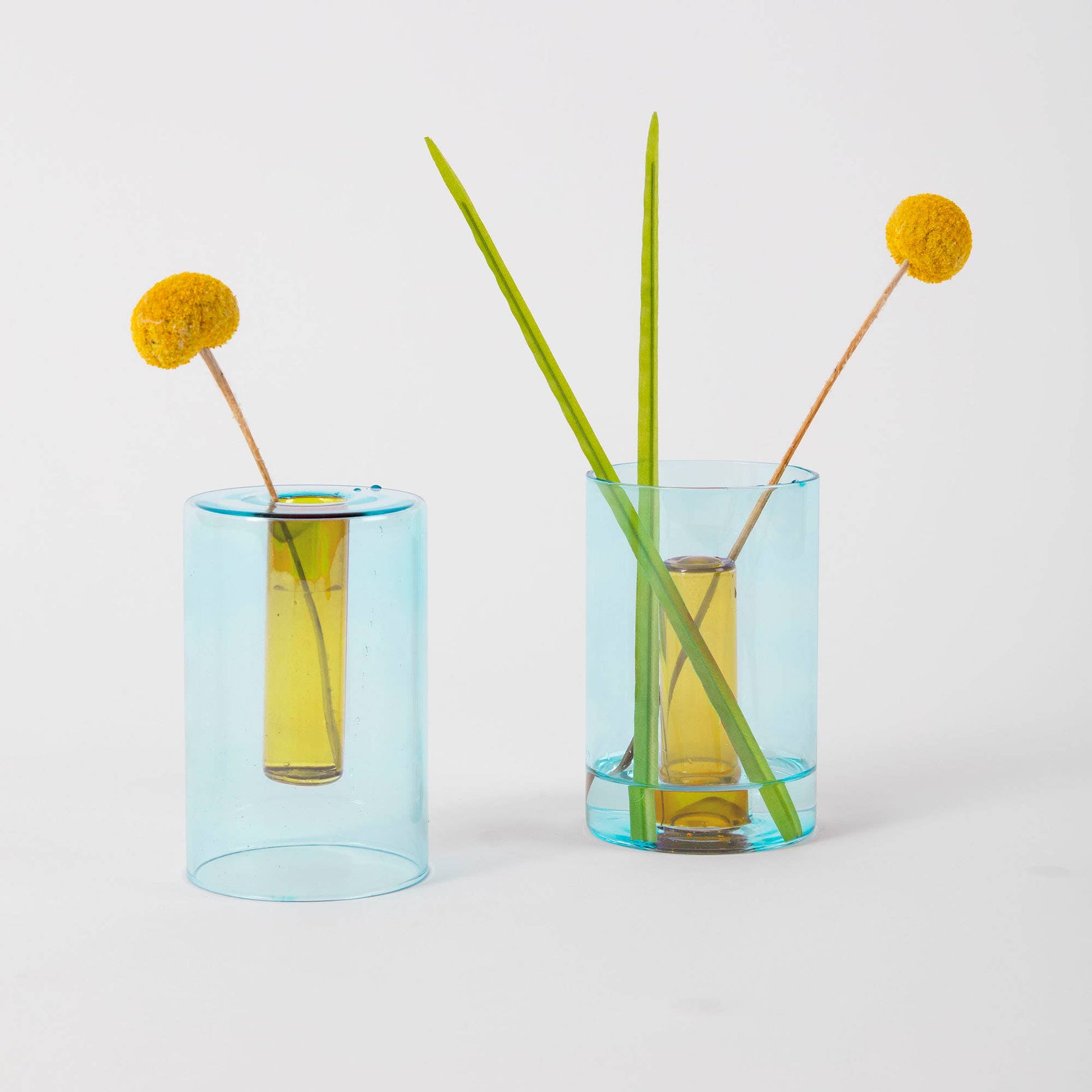 Two blue glass vases with yellow flowers and green stems on a light gray background