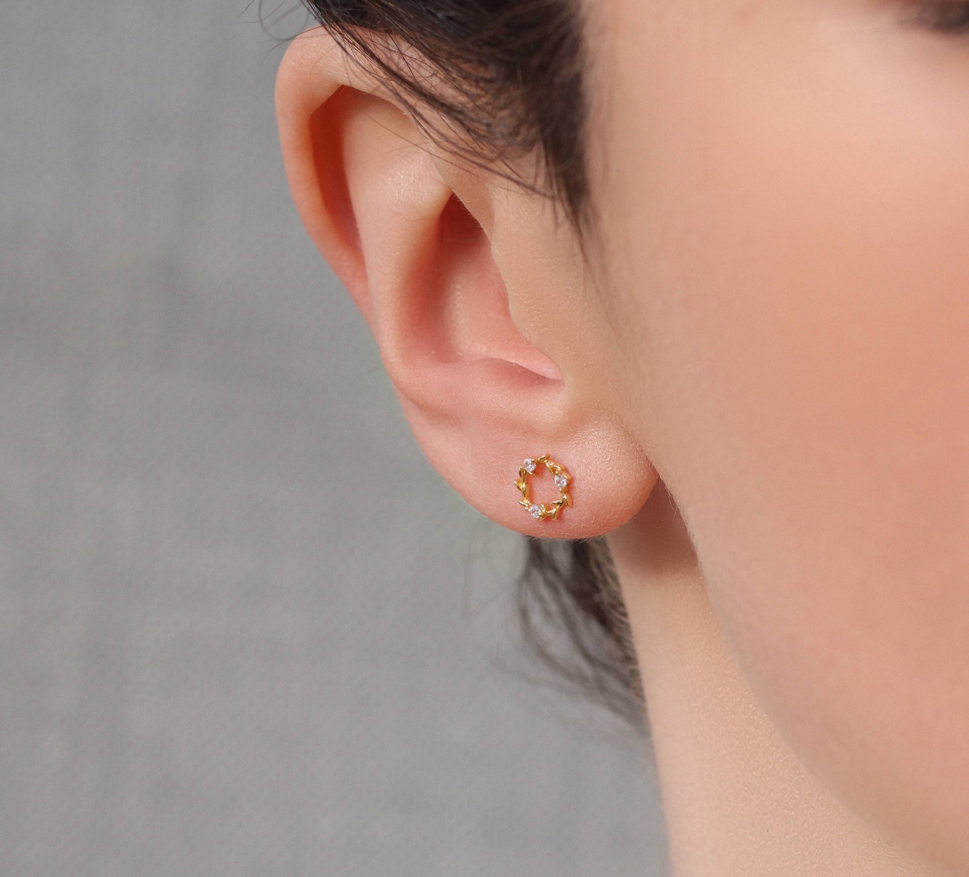 Model wears unusual stud earrings feature a miniature laurel leaf design, with cubic zirconia crystals formed to create a fluid, Art Nouveau inspired design. 
