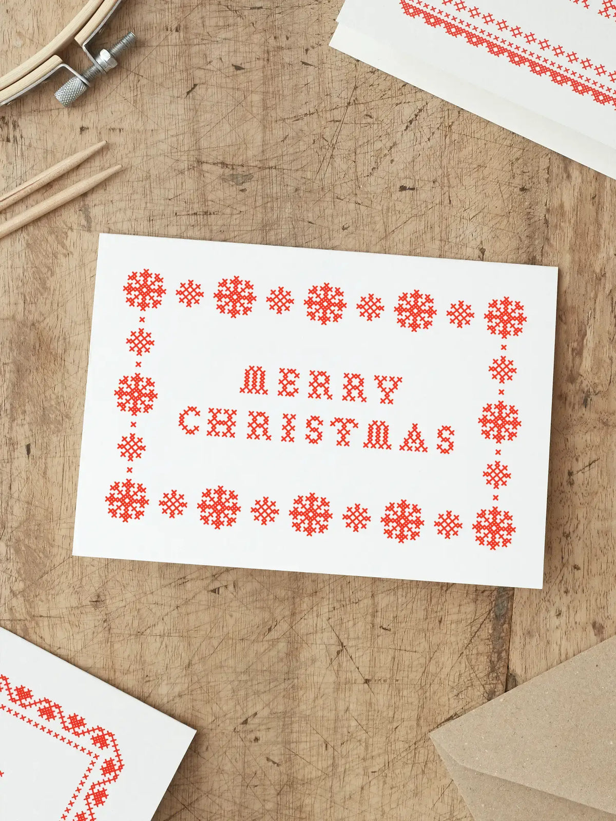 Hand-printed red cross stitch Christmas card with snowflake border