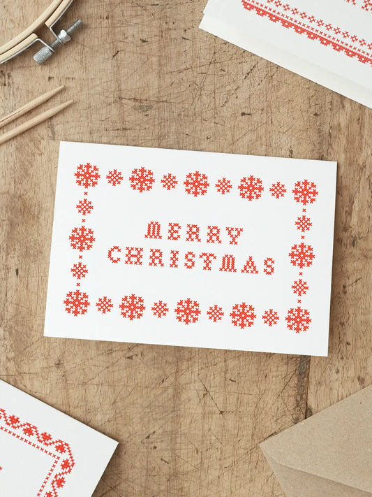 Hand-printed red cross stitch Christmas card with snowflake border