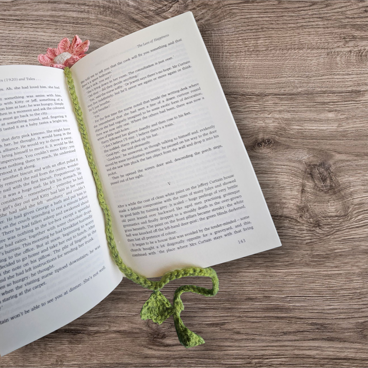 Open book with a pink flower and green stemmed crochet bookmark on a wooden surface