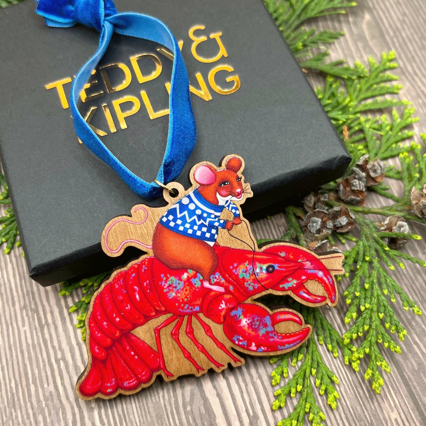 Mouse On A Lobster wooden Christmas tree decoration with Teddy & Kipling illustration, sustainably certified cherry wood, gold-plated ring, and royal blue velvet ribbon.