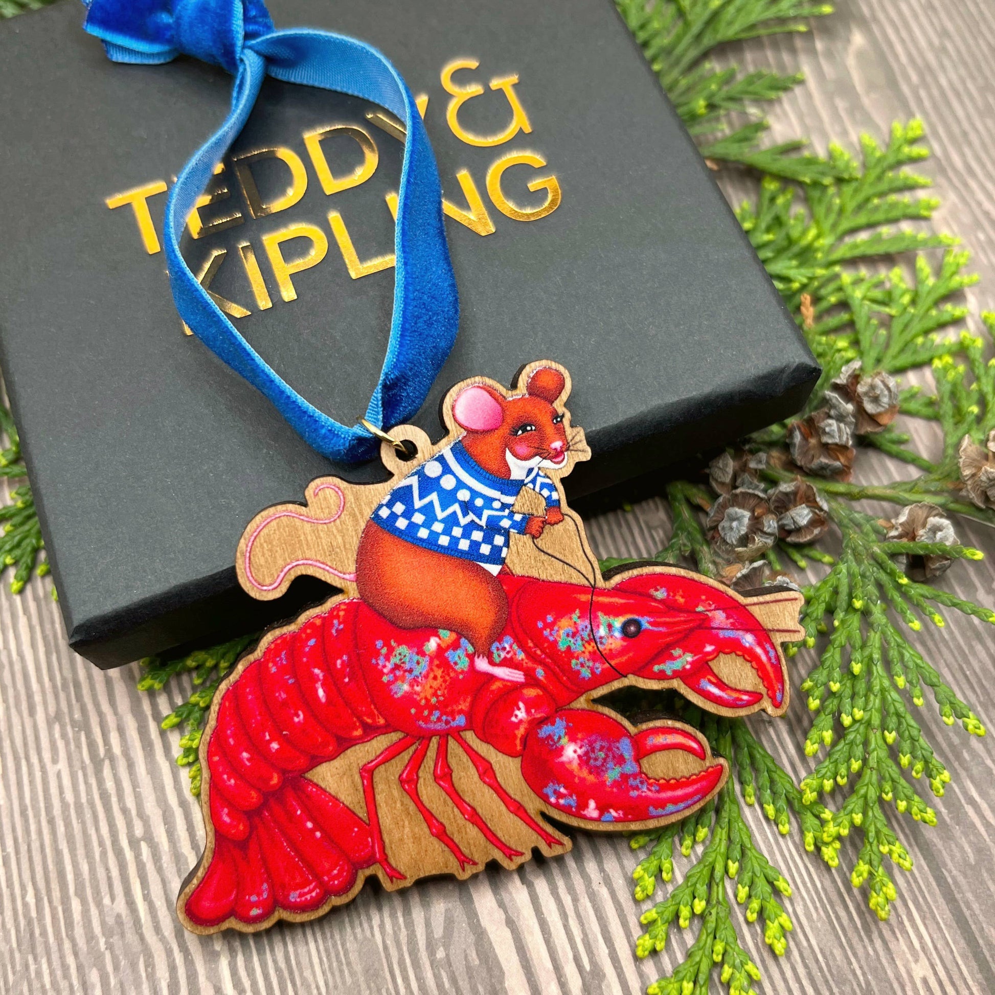 Mouse On A Lobster wooden Christmas tree decoration with Teddy & Kipling illustration, sustainably certified cherry wood, gold-plated ring, and royal blue velvet ribbon.