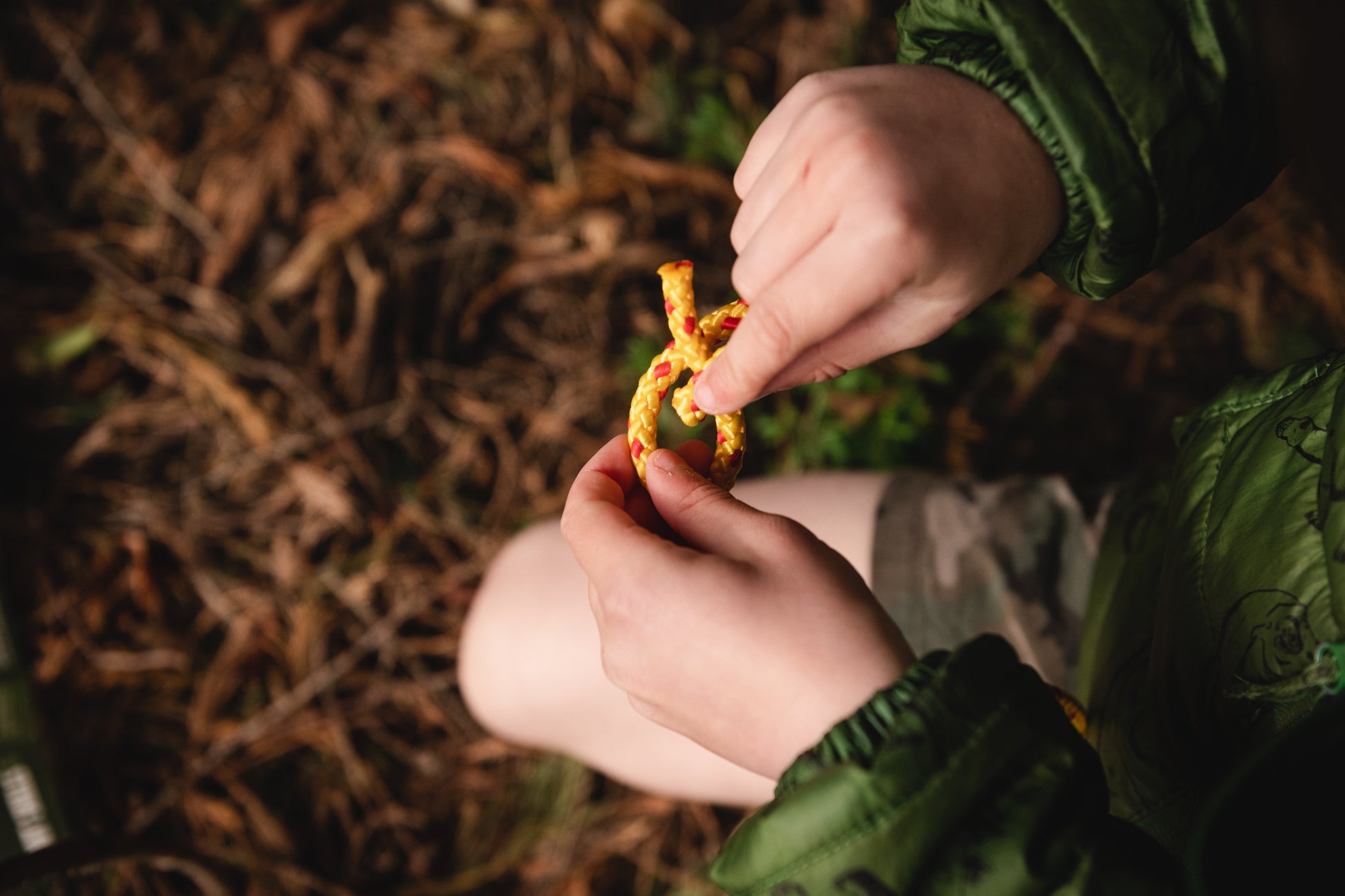 Shows a child's hands learning to tie one of the knots with yellow and red cordage.