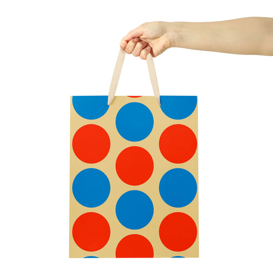 Hand holding a paper bag with blue and red polka dots on a white background