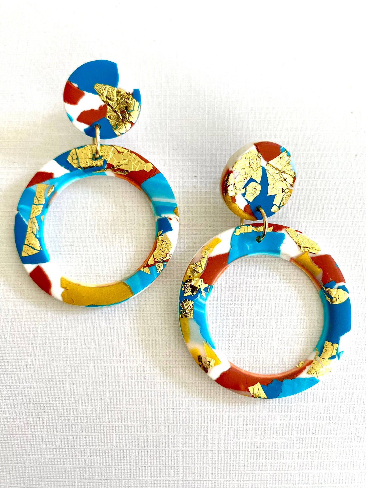 Large polymer clay hoop earrings with turquoise, teal, white and terracotta colours, and splashes of gold leaf.