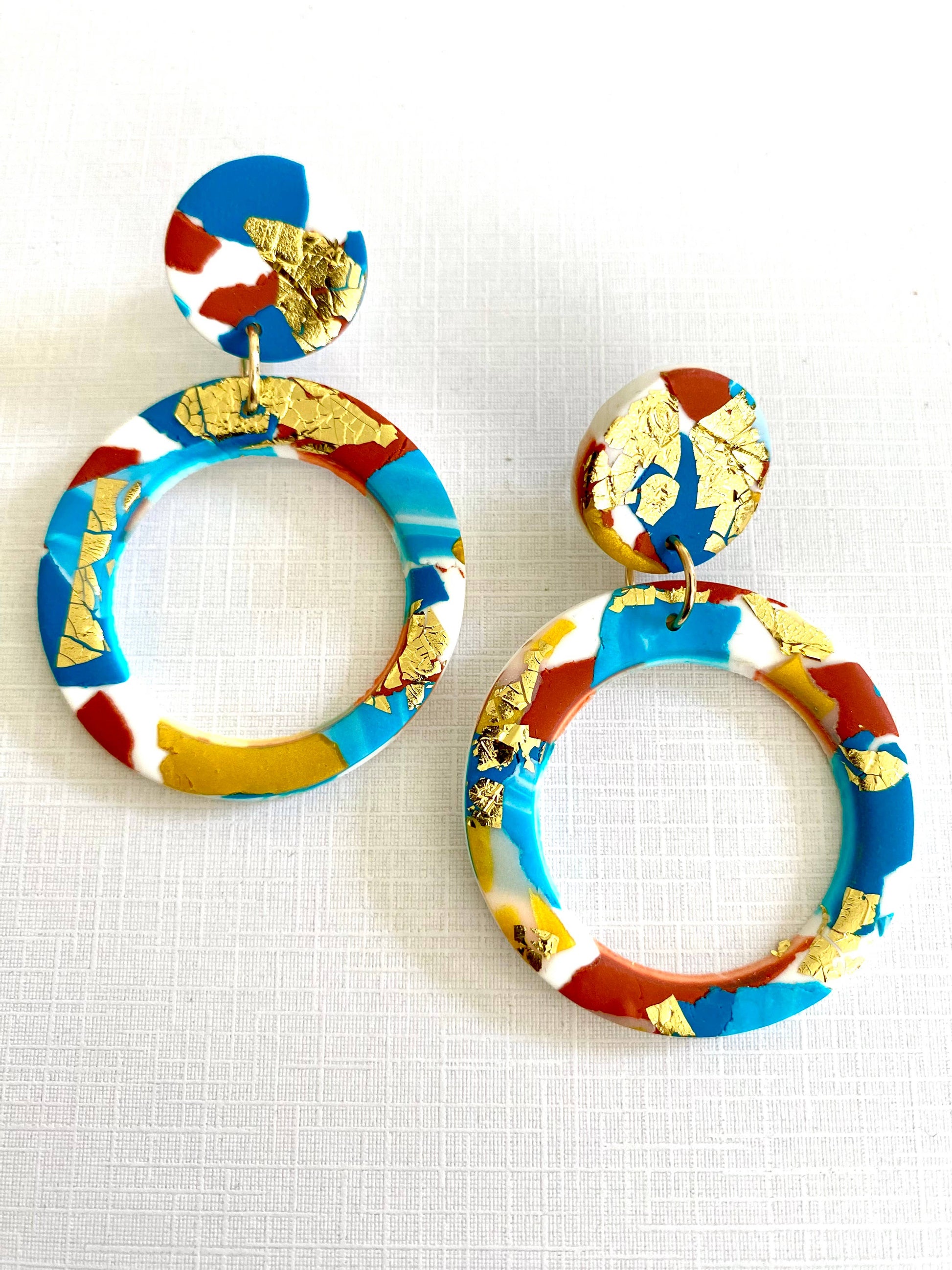 Large polymer clay hoop earrings with turquoise, teal, white and terracotta colours, and splashes of gold leaf.