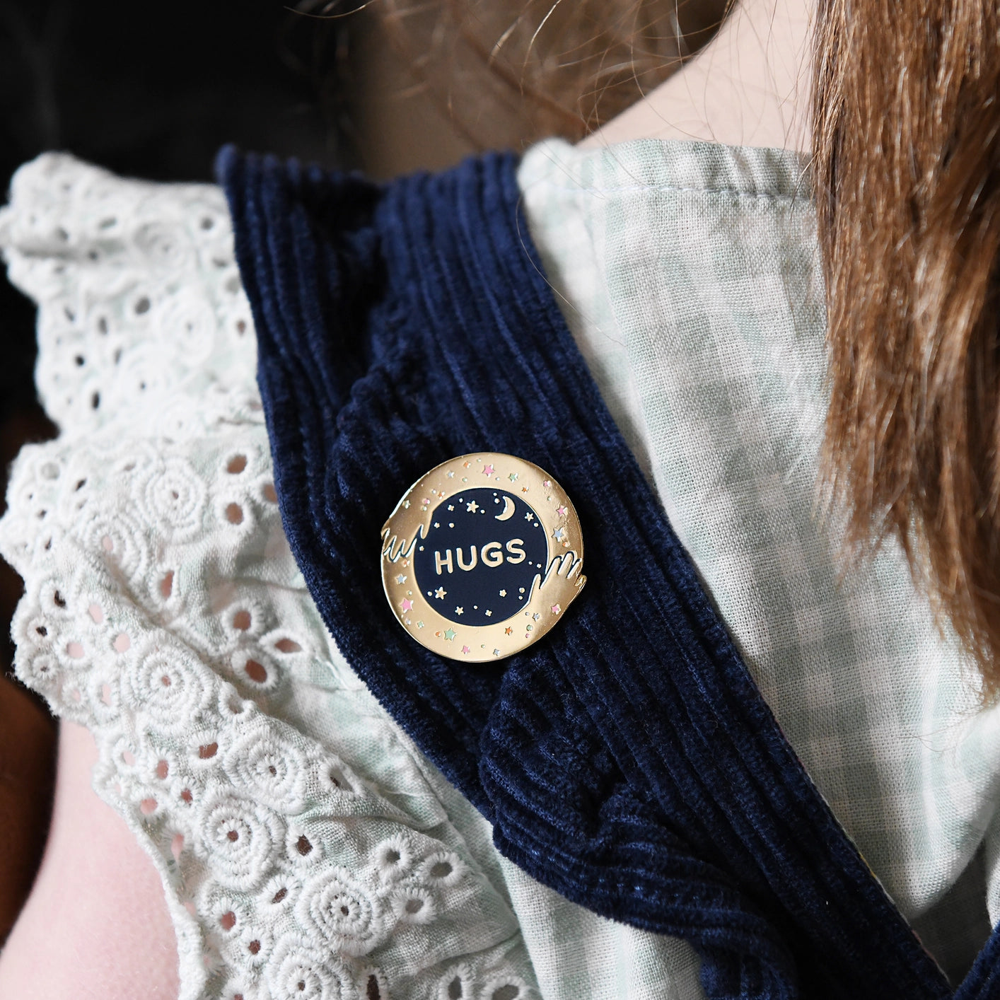 Person wearing a navy blue sweater with a 'HUGS' button on a white lace garment.