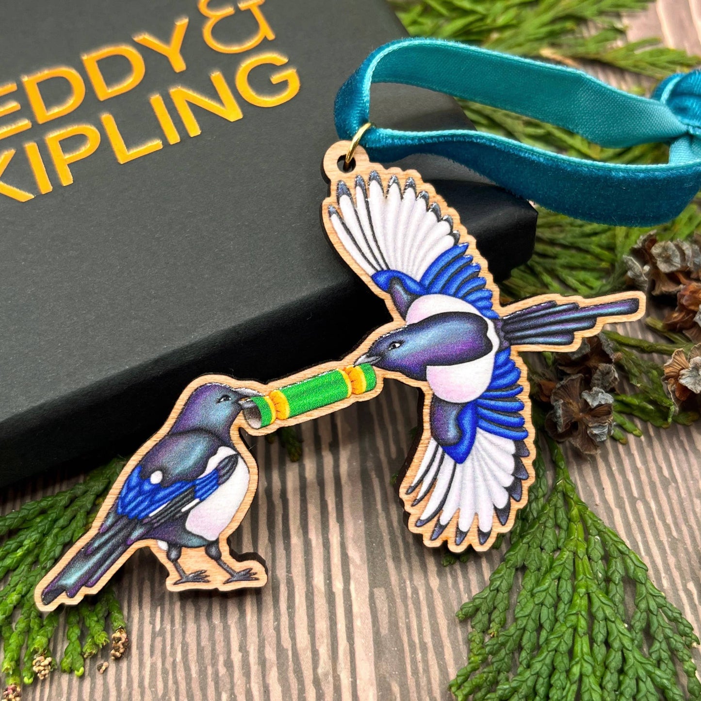 Magpie wooden Christmas tree decoration featuring Teddy & Kipling illustration, sustainably certified cherry wood, gold-plated ring, and dark teal velvet ribbon