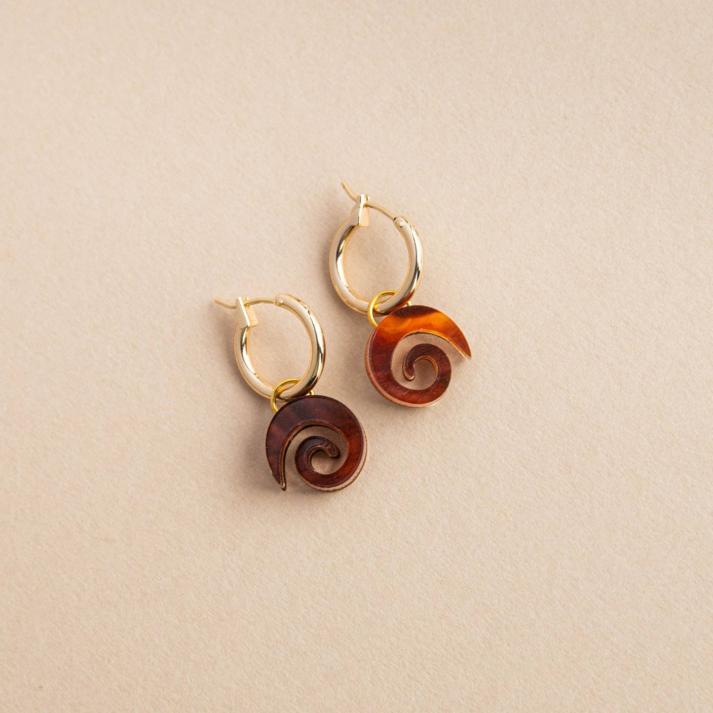 Close-up of Swirl Gold Hoop Earrings, featuring a minimalist swirl design in acrylic and sustainably sourced wood, with a gold-plated brass hoop.