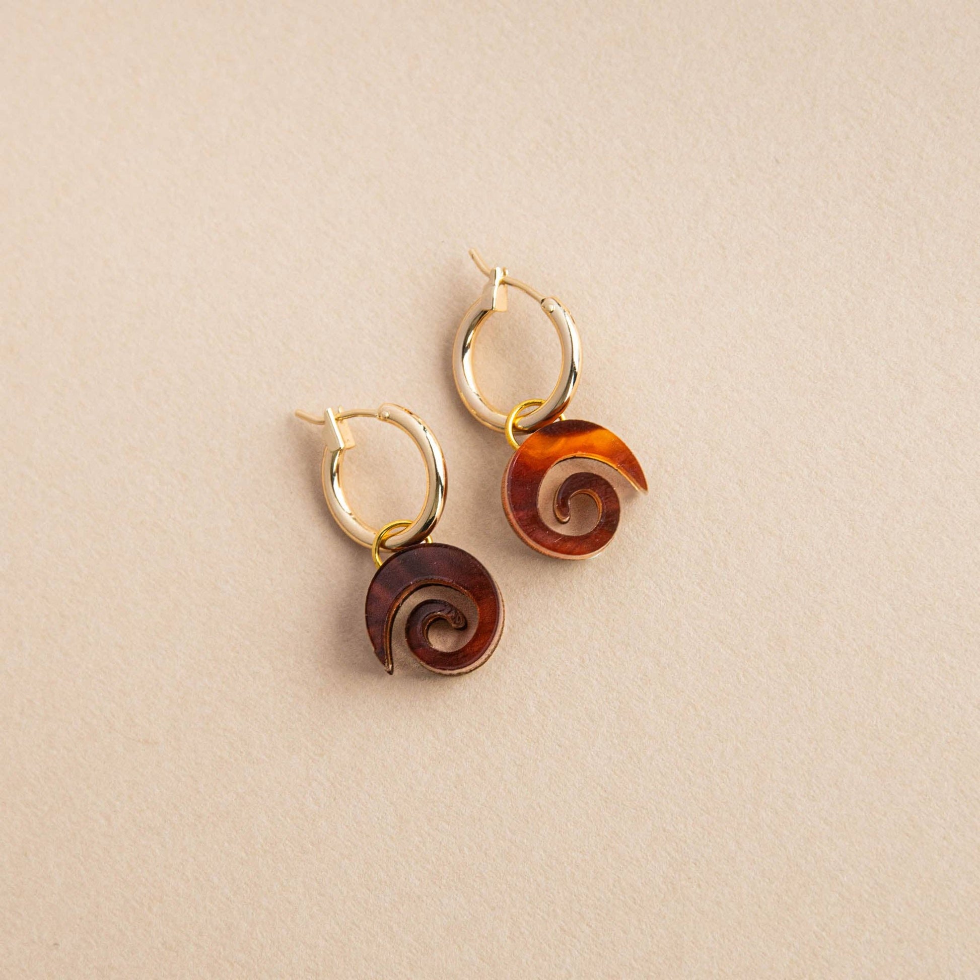 Close-up of Swirl Gold Hoop Earrings, featuring a minimalist swirl design in acrylic and sustainably sourced wood, with a gold-plated brass hoop.