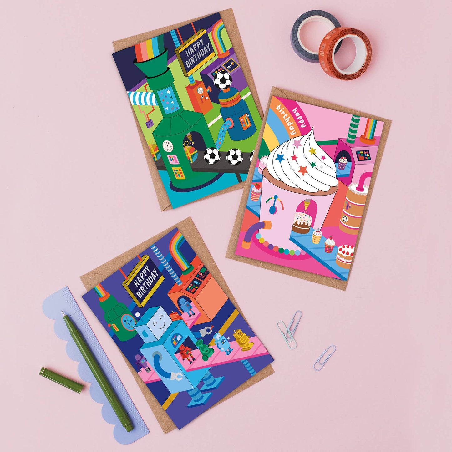 Three colorful Mifkins birthday cards on a pink background with stationery items.