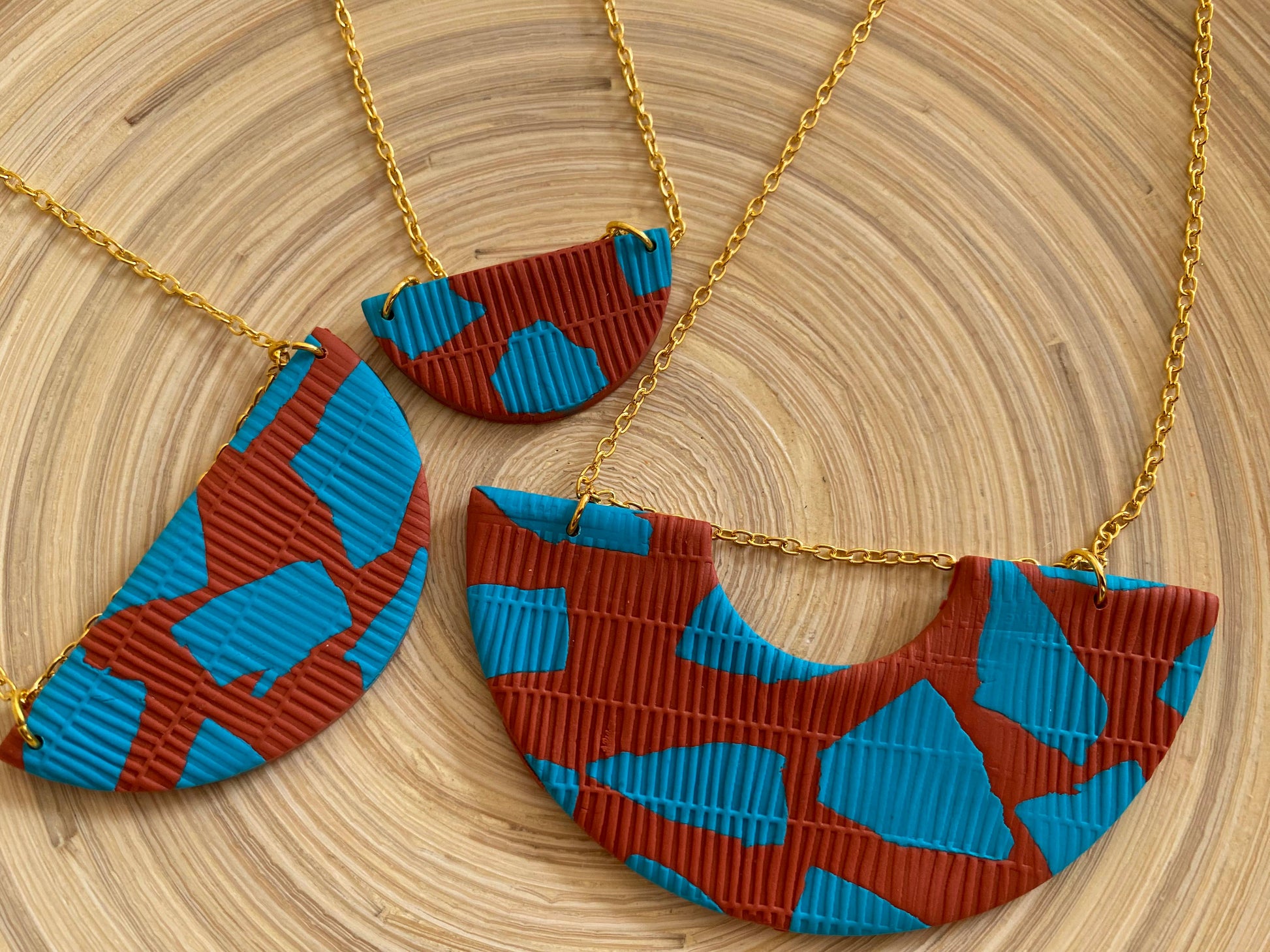 Handmade polymer clay necklace with gold leaf. No two pieces are ever exactly the same as they are all cut from a large designed piece of clay. Abstract shapes in turquoise and the background is terracotta. On a 22ct gold-plated brass chain. 