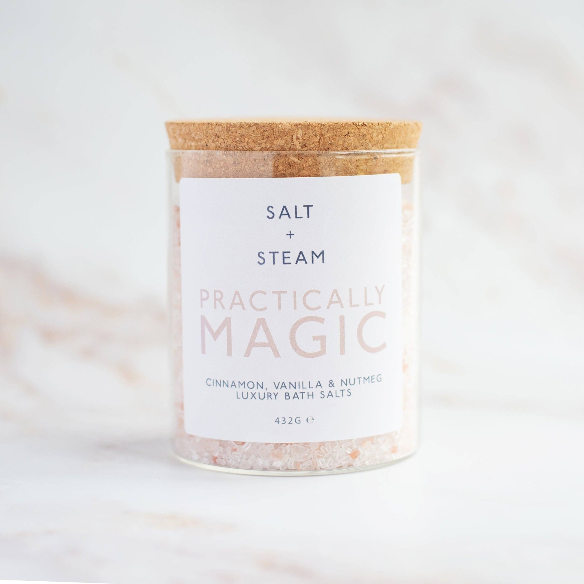 Jar of 'Practically Magic' bath salts with a cork lid on a white background