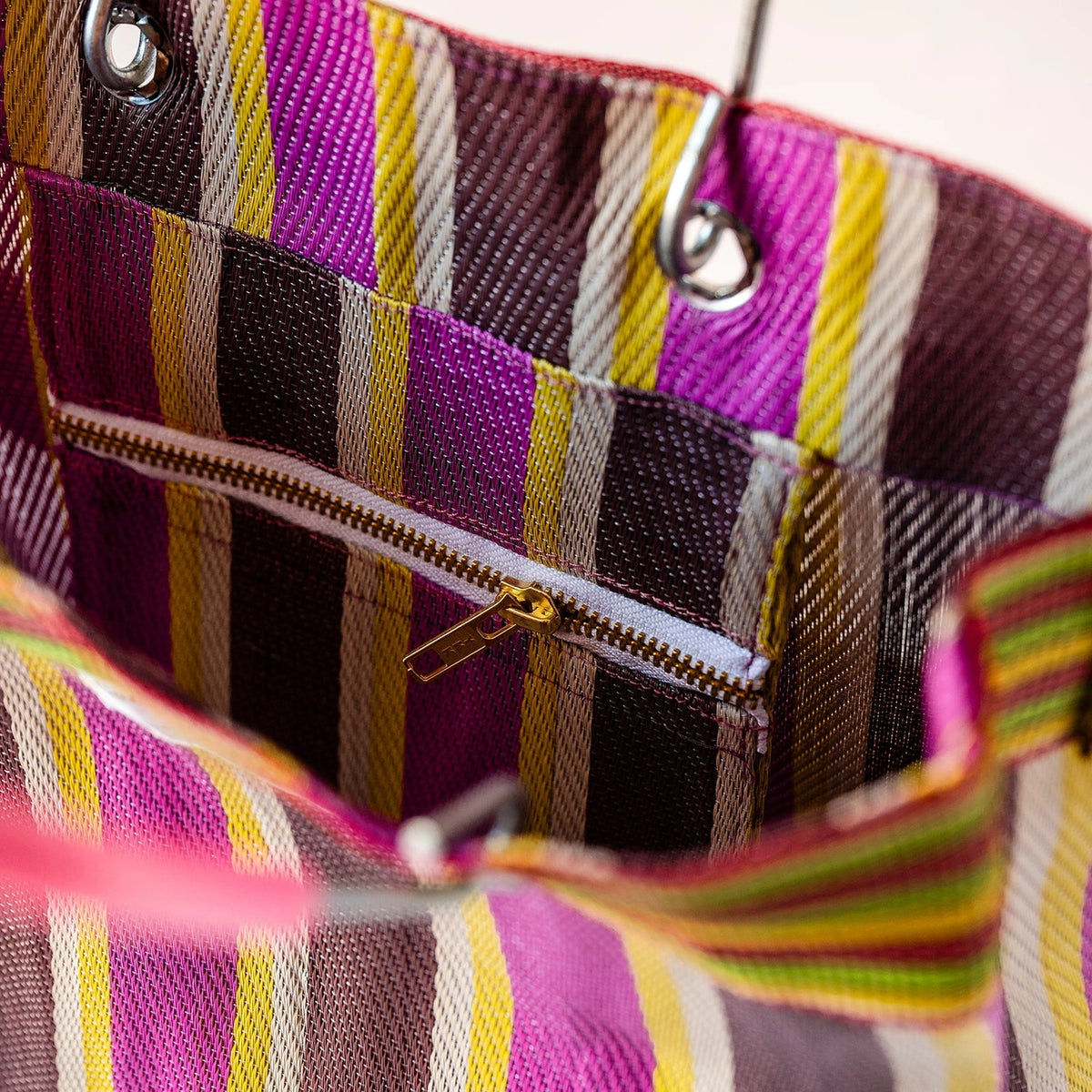 Close-up of a striped fabric tote bag interior with a zippered pocket, featuring pink, purple, yellow, brown, and white vertical stripes.