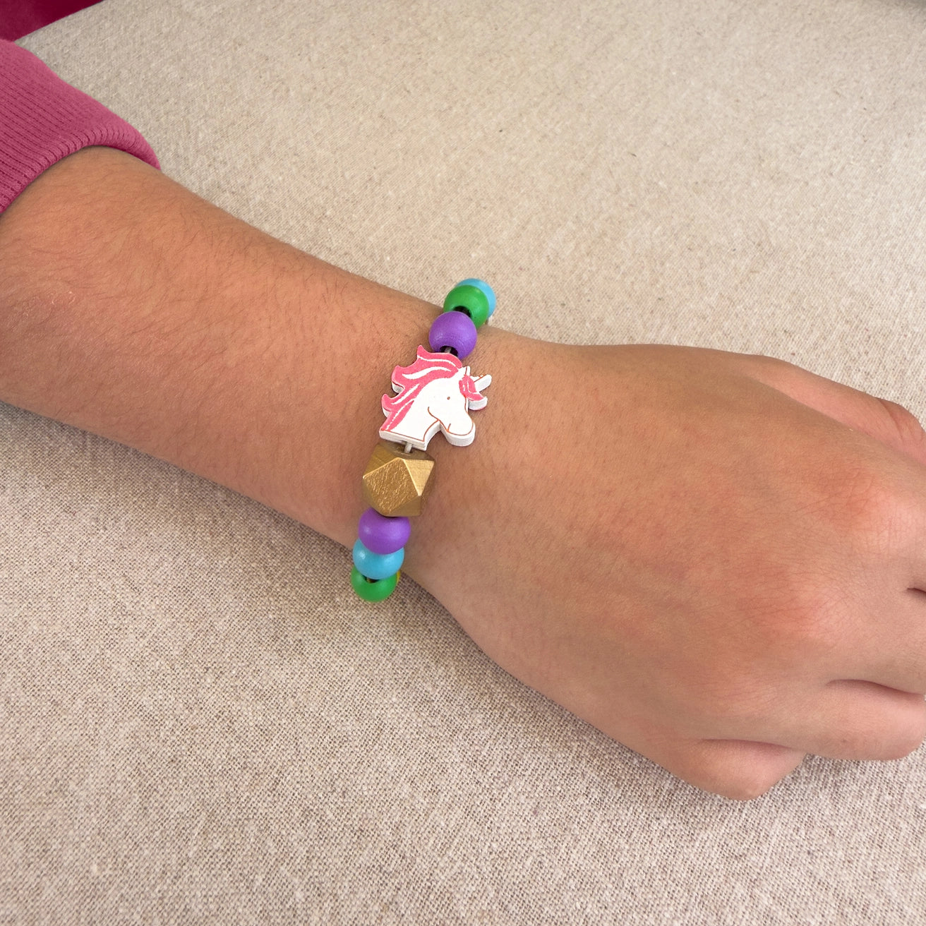 Colorful bracelet with a unicorn charm on a wrist against a beige background