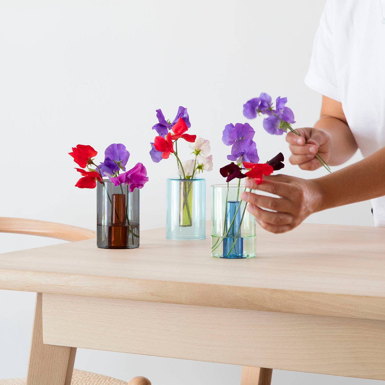 Person arranging flowers in small glass vases on a wooden table.