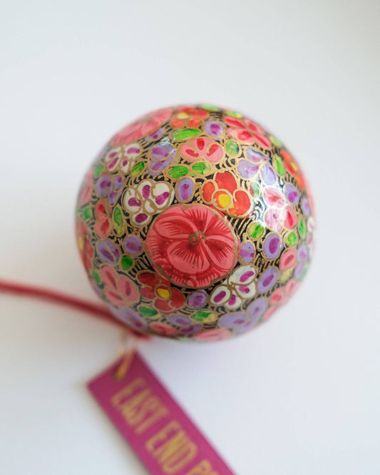 Gold Floret Papier Mâché Christmas Bauble hanging on a tree branch, showcasing its velvet loop.