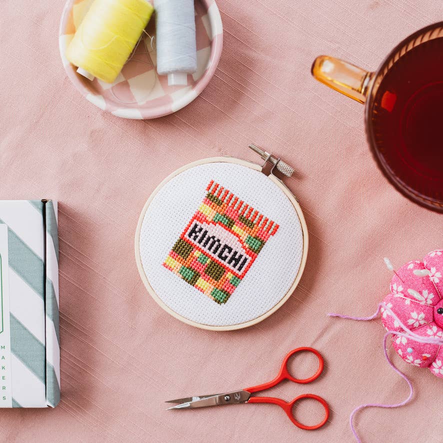 The Kimchi Mini Cross Stitch Kit's eco-friendly packaging, a striped recyclable box, clearly displaying the kit's design.