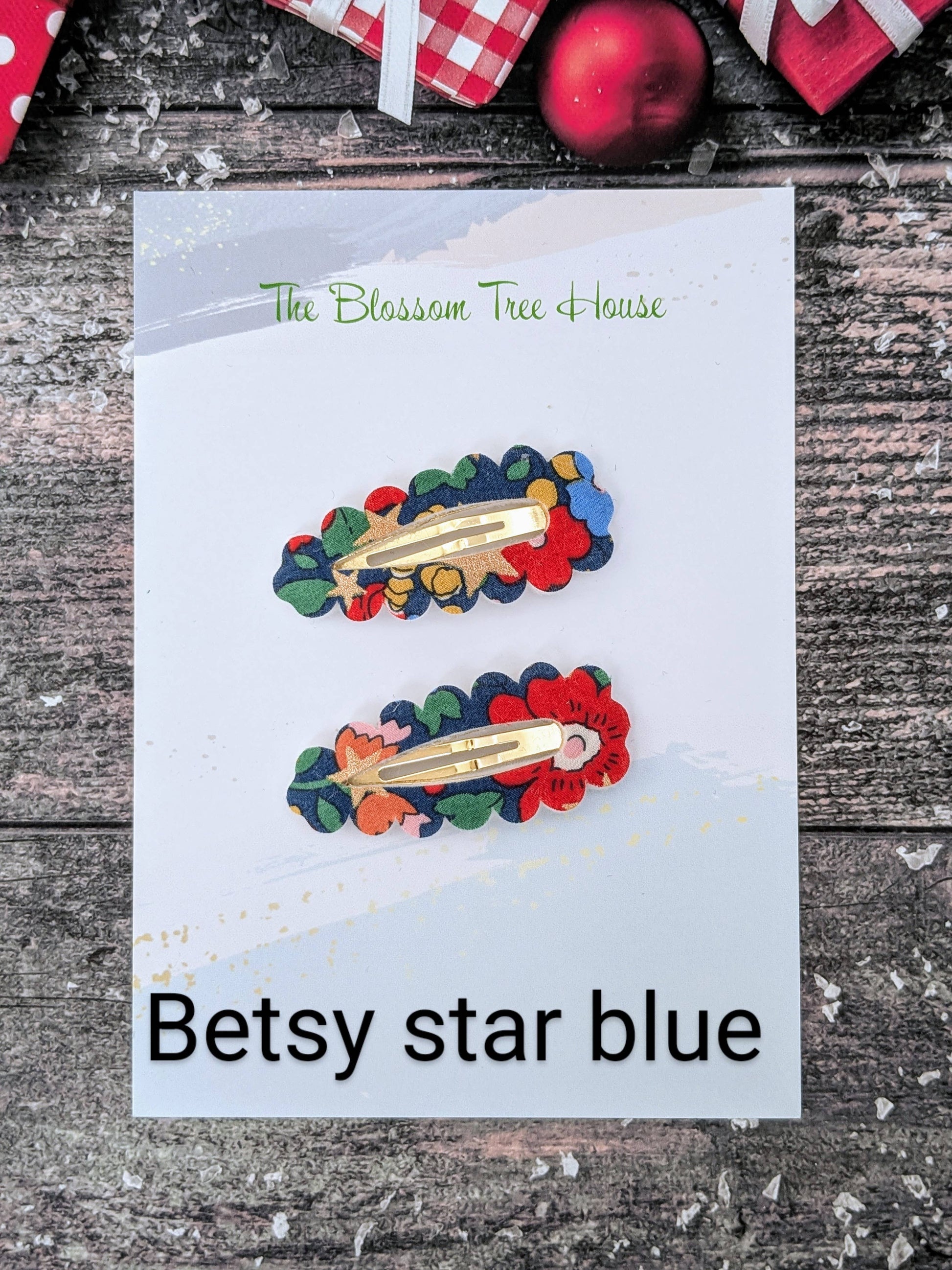 Colorful hair clips on a card with 'Betsy star blue' text, placed on a wooden surface.