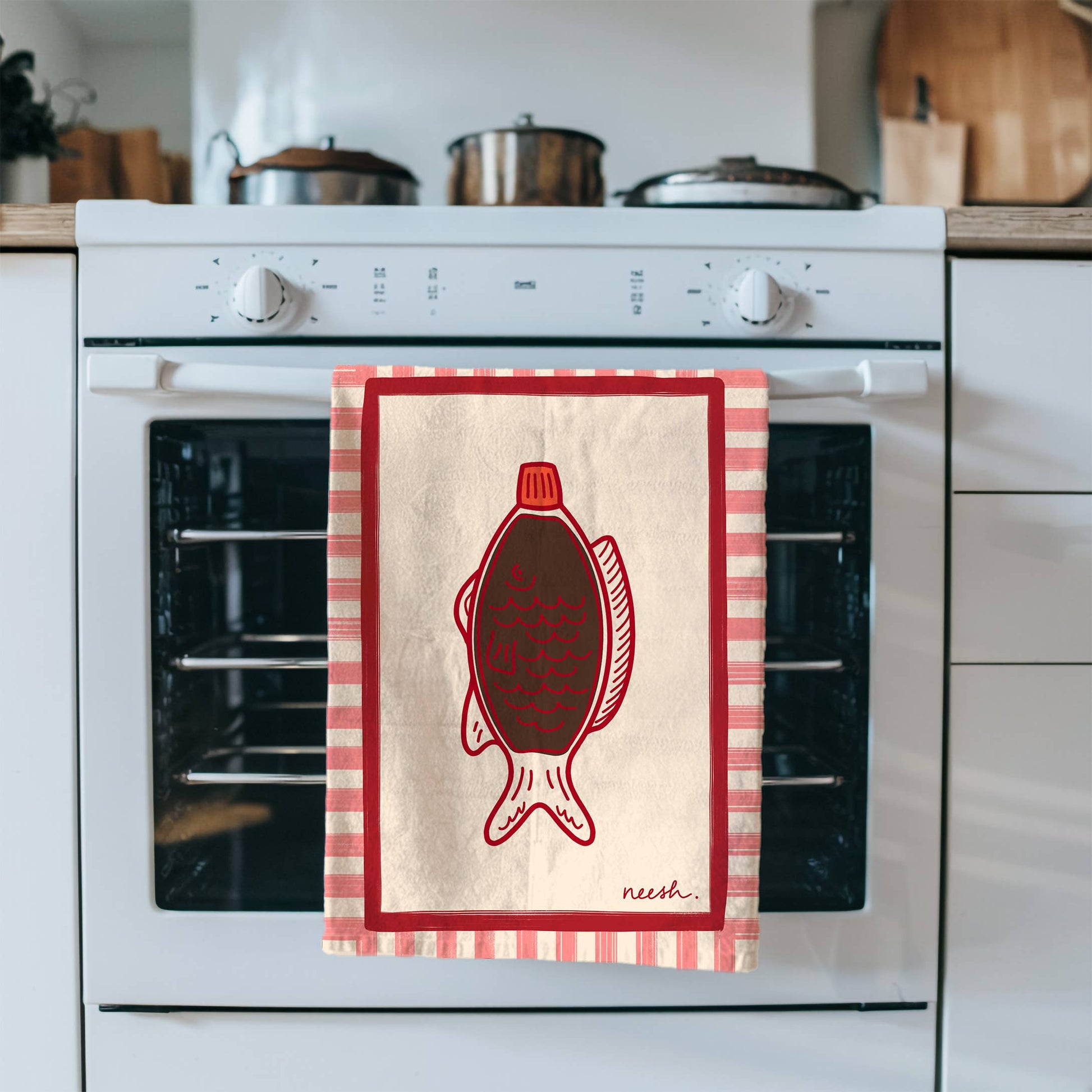 White 100% cotton tea towel featuring a black and red hand-drawn soy sauce fish bottle design, displayed in a modern kitchen setting. UK made, eco-friendly kitchen decor.