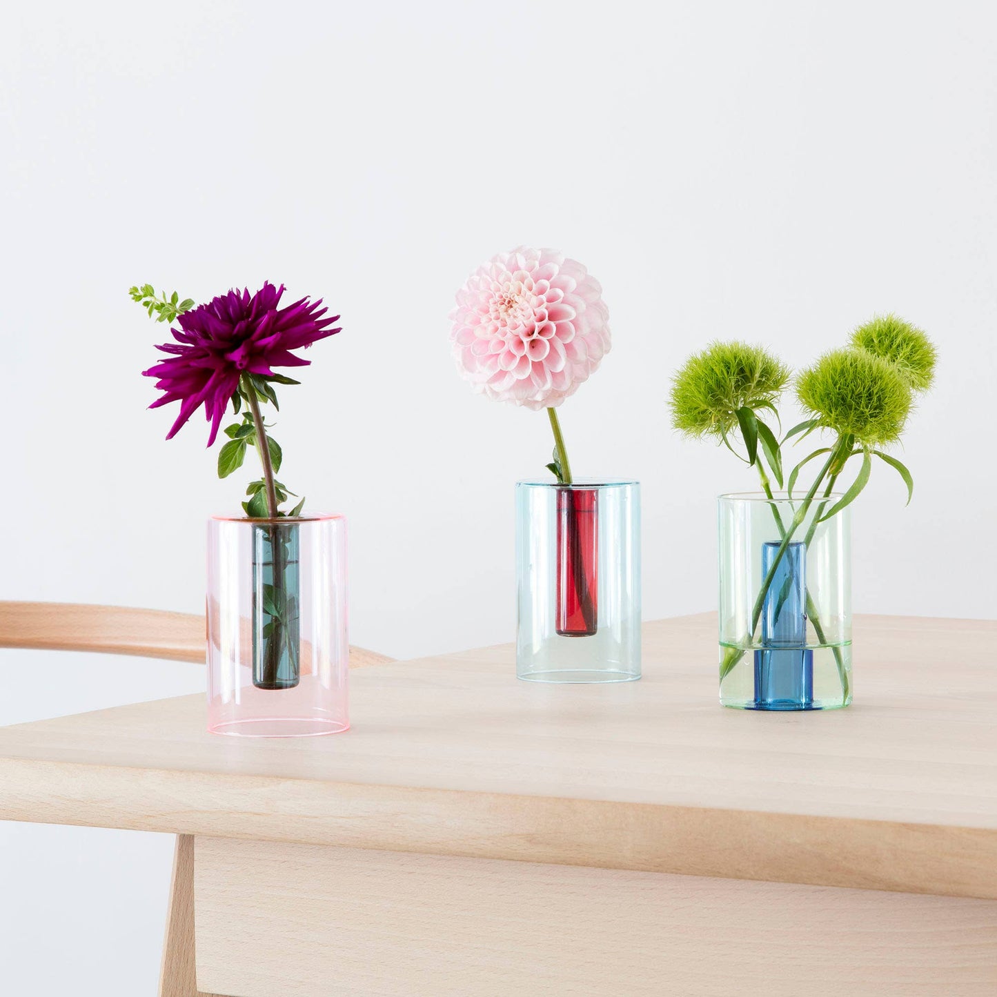 Three transparent vases with flowers on a wooden table against a white background