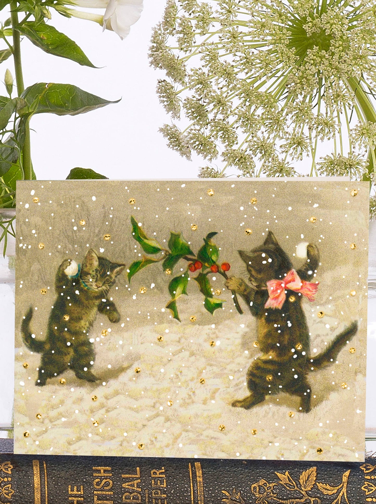 A glittery snow scene sets the stage for a playful card, featuring two frolicking kittens engaged in a snowball fight. Vintage inspiration adds an extra touch of charm.