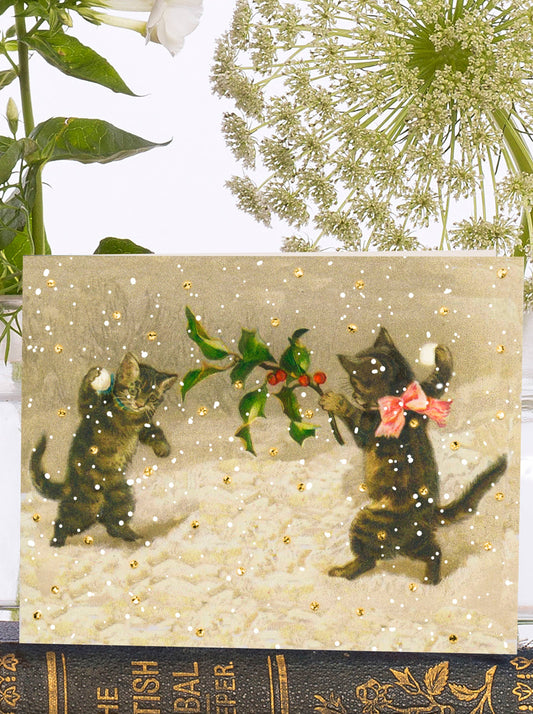 A glittery snow scene sets the stage for a playful card, featuring two frolicking kittens engaged in a snowball fight. Vintage inspiration adds an extra touch of charm.