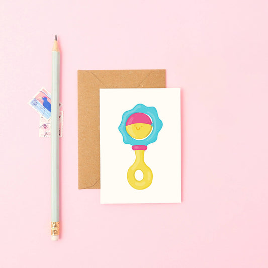 Hand-drawn baby rattle mini card with a cute face in blue, pink, and yellow