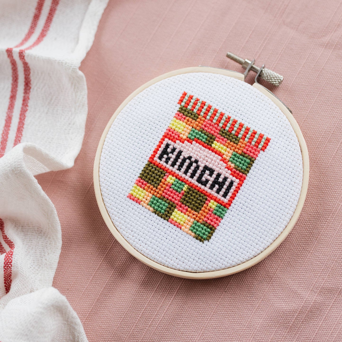 Kimchi Mini Cross Stitch Kit box with some contents like the wooden hoop and threads playfully peeking out.