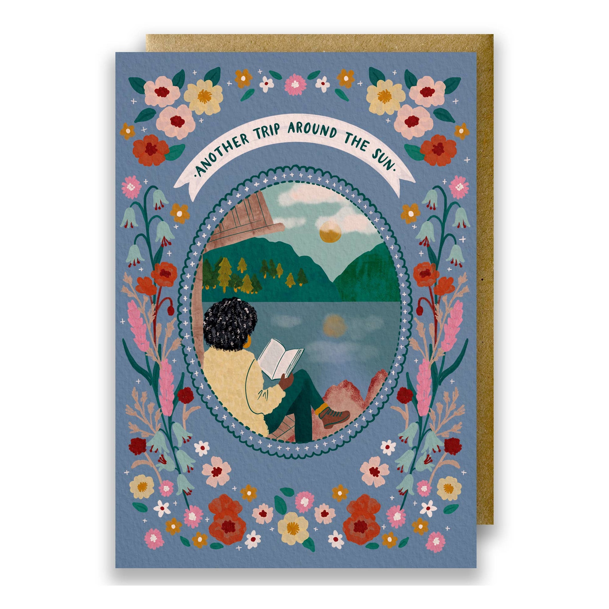 Wild Adventure Another Trip Around The Sun birthday card featuring a woman reading by a lakeside cabin