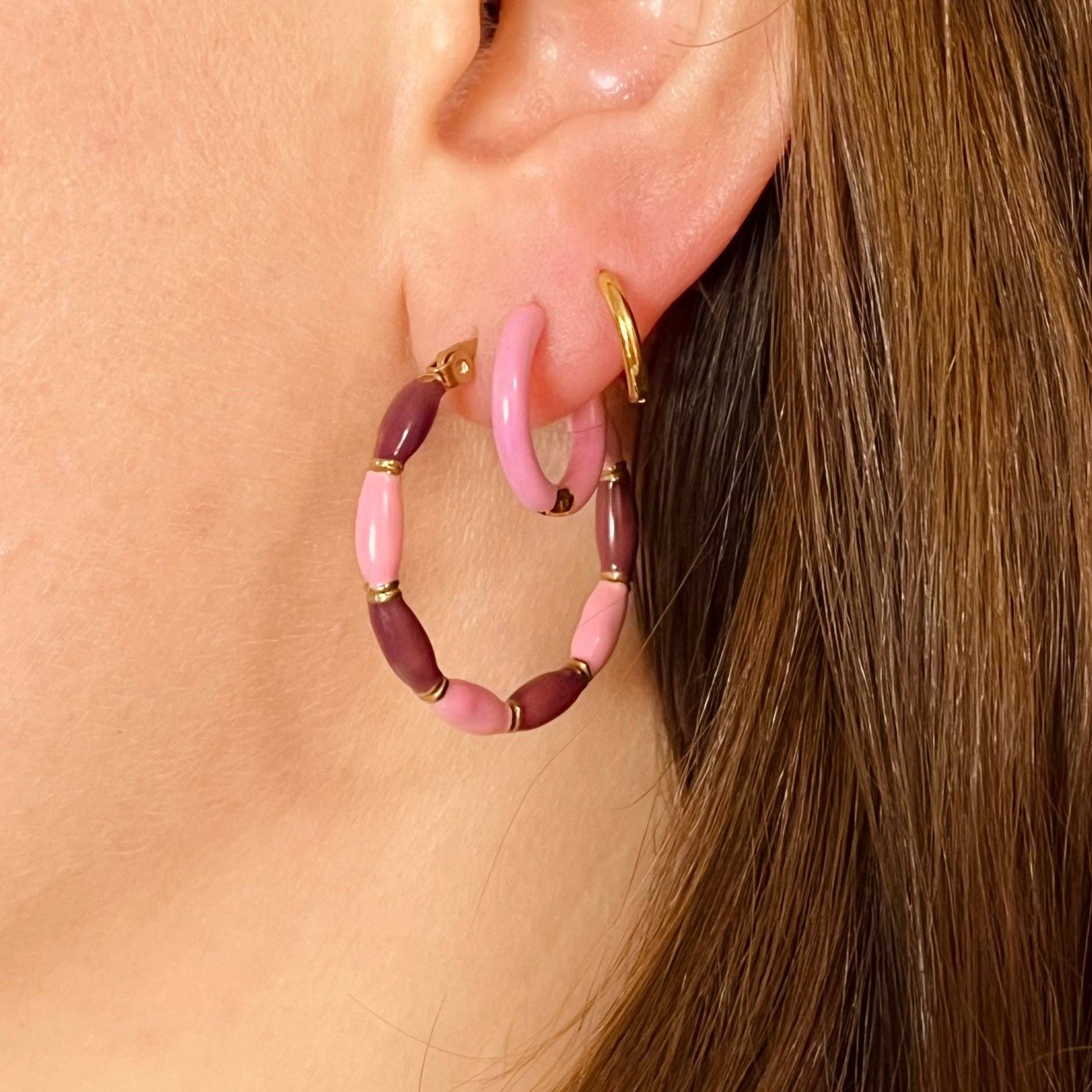 Gold plated Hoop with candy stripes enamel plating, shown in Pink + Maroon. Along with two other smaller hoops on a person's ear lobe.