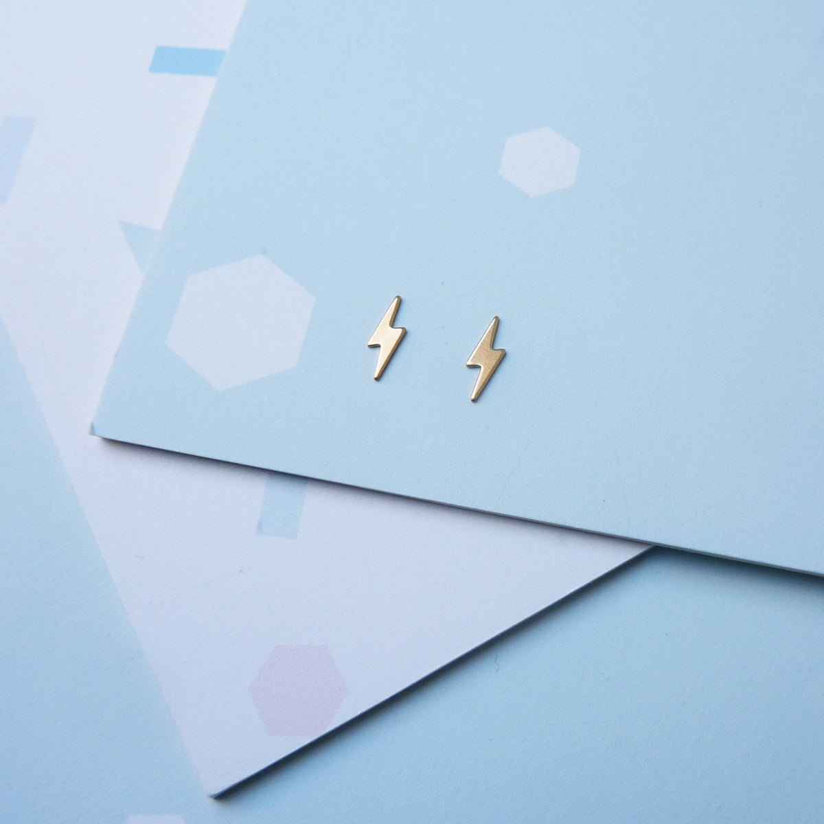 Pair of tiny gold lightning bolt earrings showing scroll backs