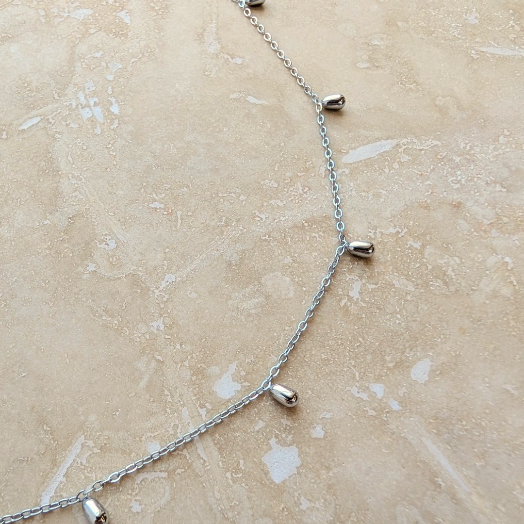 Minimalist silver droplet necklace on a display card