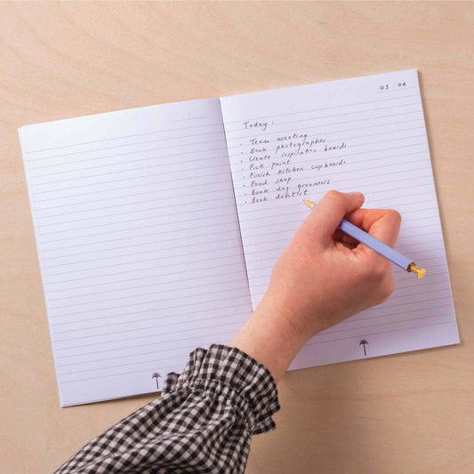 Hand writing in a notebook with a pen on a beige surface