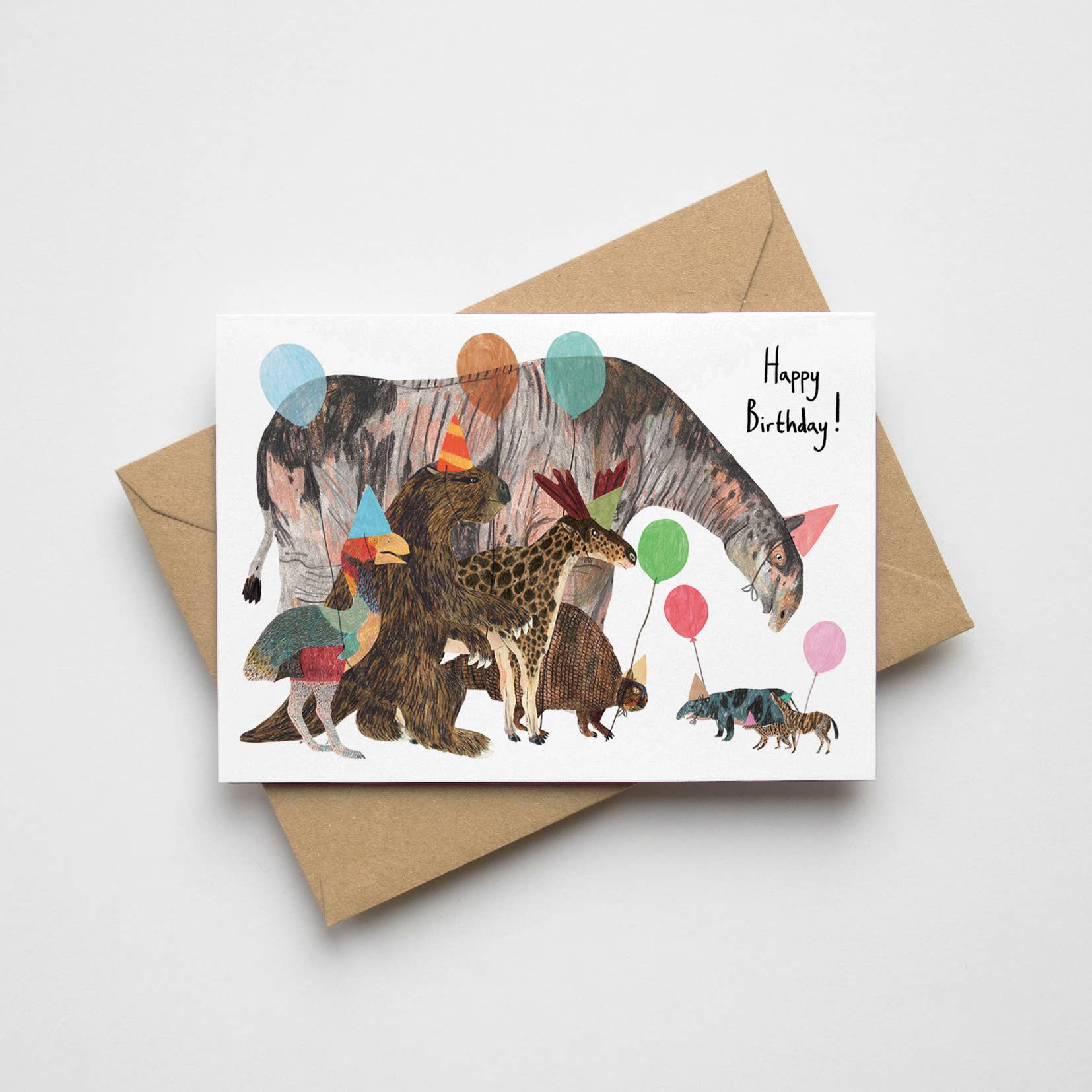 Hand-illustrated prehistoric birthday card featuring cartoon prehistoric mammals and a bird in party hats with balloons. A6 size, UK printed, blank inside.