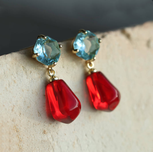 These sweet and colourful earrings feature a light sapphire blue glass jewel in a delicate, with a bright red pomegranate seed charm beneath.  These earrings have a stud post fastening with butterfly backs. The blue jewels are made from glass and the pomegranate seeds are made from resin. They measure 30mm (just over one inch) in length and are light and comfortable to wear.