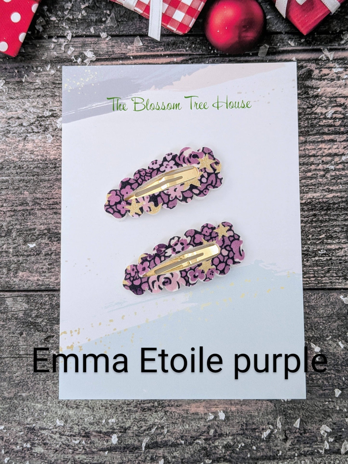Purple hair clips with gold accents on a card labeled 'Emma Etoile purple' against a rustic wooden background.