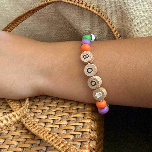 Child's hands crafting a Halloween ghost bracelet from the Cotton Twist kit, showcasing vibrant wooden beads