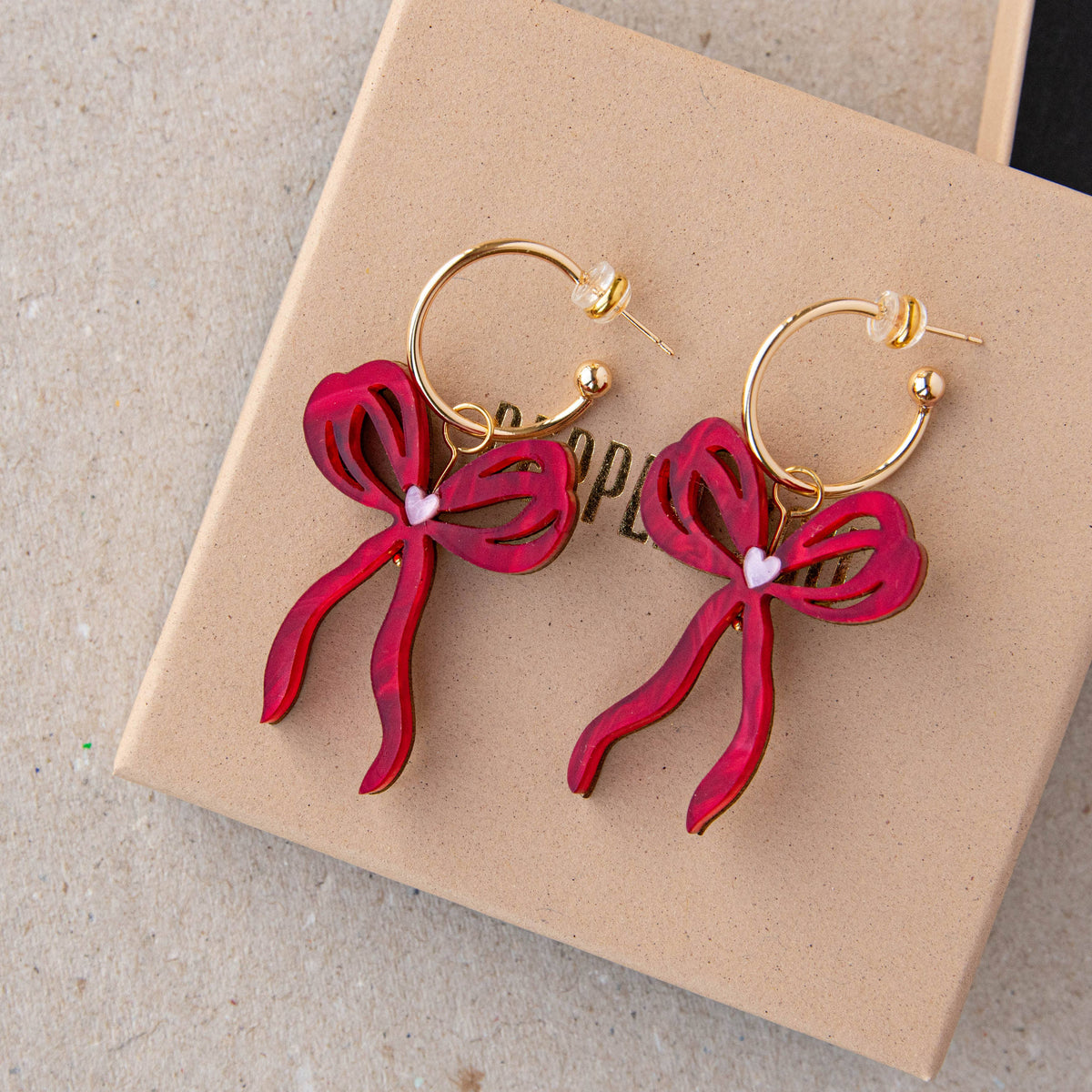 Close up of laser cut bow hoop earrings on gold plated posts
